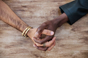 Gay couple holding hands over wooden table at sidewalk cafe - AGOF00126