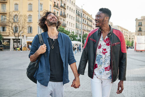 Happy gay couple with holding hands walking on road - AGOF00128