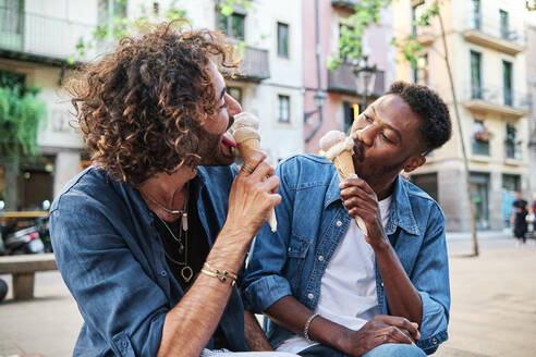 Gay couple eating ice cream while looking at each other - AGOF00132