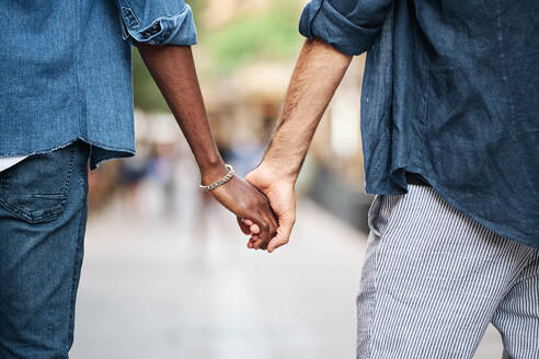 Affectionate gay couple holding hands while walking - AGOF00136