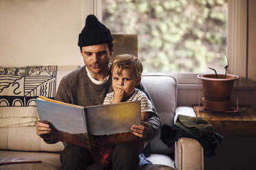 Vater liest seinem Sohn eine Geschichte vor, während er zu Hause auf dem Sofa sitzt - ACTF00039