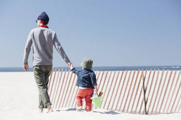 Vater und Sohn halten sich an den Händen, während sie an einem sonnigen Tag am Strand spazieren gehen - ACTF00041