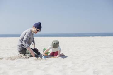 Mann und Sohn spielen mit Sandspielzeug am Strand an einem sonnigen Tag - ACTF00048