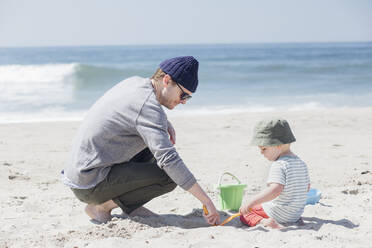 Mann und Sohn spielen mit Sandspielzeug am Wasser am Strand - ACTF00055