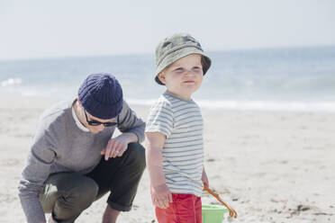 Niedlicher kleiner Junge, der wegschaut, während er neben seinem Vater am Strand steht - ACTF00056