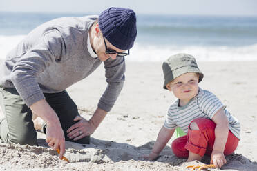 Vater gräbt Sand, Sohn mit Hut schaut weg - ACTF00058