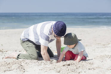 Vater und Sohn graben gemeinsam im Sand, während sie an einem sonnigen Tag am Strand spielen - ACTF00059