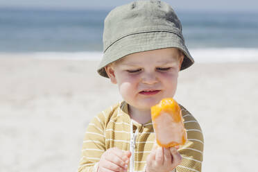 Cute little boy wearing hat having ice cream at beach during sunny day - ACTF00063