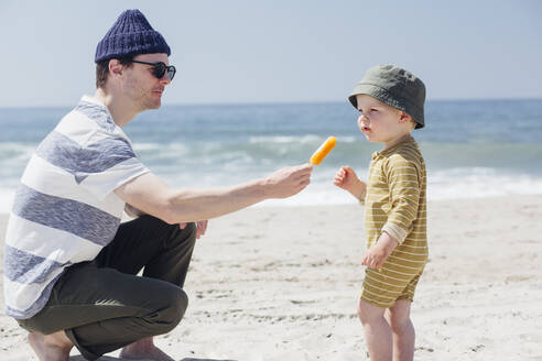 Mann mit Sonnenbrille füttert seinen Sohn am Strand mit Eiscreme - ACTF00064