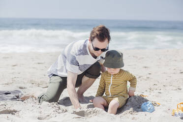 Vater und Sohn spielen mit Sand am Strand an einem sonnigen Tag - ACTF00074