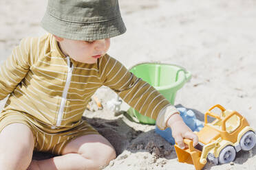 Junge spielt mit Spielzeugauto, während er am Strand im Sand sitzt - ACTF00076