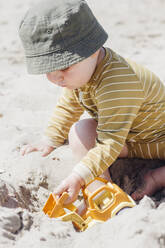 Boy sitting on sand playing with toy car at beach - ACTF00077