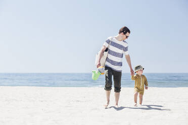 Vater und Sohn halten sich an den Händen, während sie am Strand spazieren gehen - ACTF00079