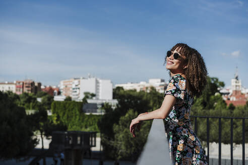 Lächelnde junge Frau mit Sonnenbrille an einem Geländer - EBBF03801