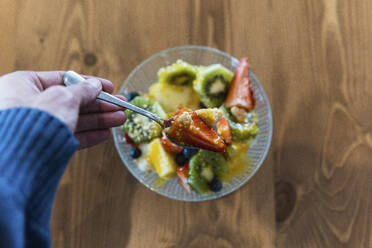 Männerhand hält Löffel beim Essen von Obstsalat im Restaurant - PNAF01779