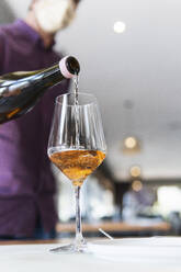Kellner schenkt im Restaurant während der COVID-19 Wein in ein Glas ein - PNAF01783