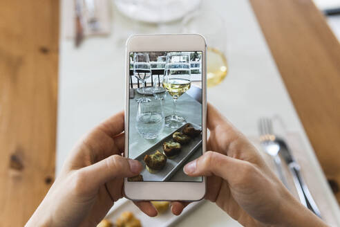 Junge Frau fotografiert Essen mit ihrem Smartphone im Restaurant - PNAF01790