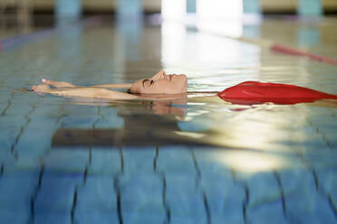 Woman with eyes closed floating on water in swimming pool - JSMF02232