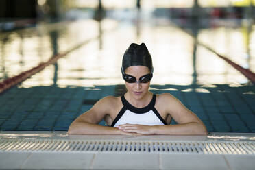 Weibliche Sportlerin mit Schwimmbrille am Beckenrand im Fitnessstudio - JSMF02250