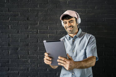 Glücklicher junger Mann mit digitalem Tablet vor einer Wand - RCPF01132