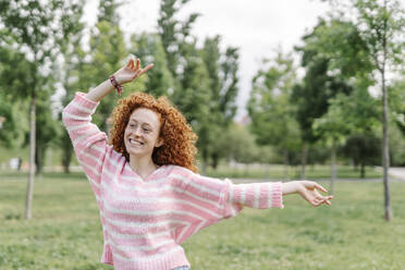 Cheerful redhead woman dancing at park - JCZF00741