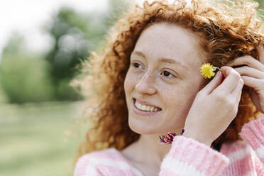 Beautiful smiling redhead woman wearing flower while looking away - JCZF00743