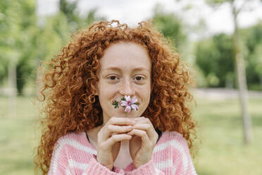 Rothaarige lockige Frau bedeckt Mund mit Blume - JCZF00748