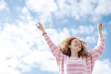 Happy redhead woman with arms raised dancing under sky - JCZF00755