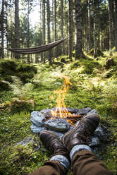Shoes of man relaxing in front of stone campfire burning in forest - HHF05621