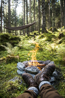 Schuhe eines Mannes, der sich vor einem Lagerfeuer aus Stein im Wald entspannt - HHF05621