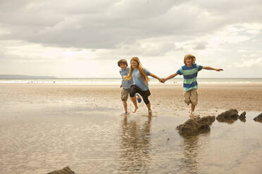 Happy friends holding hands while running at beach - AJOF01414