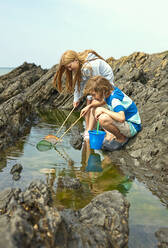 Boy and girl fishing in tidal pool at beach - AJOF01417
