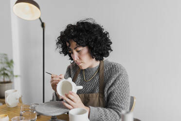 Weibliche Expertin bemalt Keramikgeschirr in der Werkstatt - ASSF00079