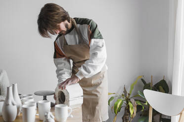 Männlicher Kunsthandwerker, der am Arbeitsplatz stehend ein Keramikmodell überprüft - ASSF00092