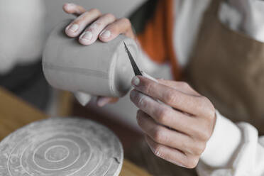 Male artist with clay cup and hand tool working at workshop - ASSF00095