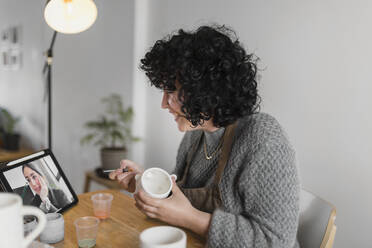 Smiling female artist with cup learning through digital tablet at workshop - ASSF00111