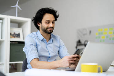 Businessman with laptop using mobile phone at office - GIOF12817