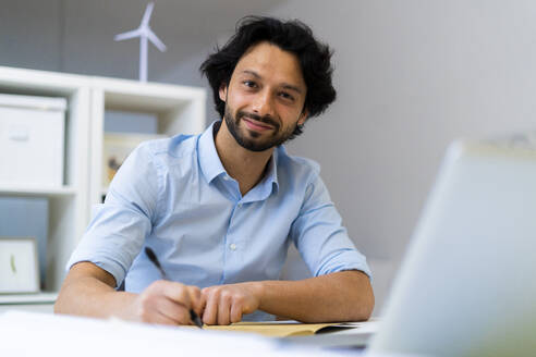 Smiling businessman sitting at desk in office - GIOF12820