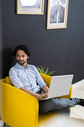 Nachdenklicher männlicher Unternehmer mit Laptop auf einem Sessel im Büro sitzend - GIOF12834