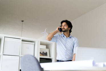 Männlicher Unternehmer, der im Büro mit einem Mobiltelefon spricht - GIOF12835