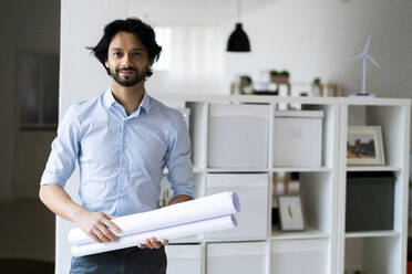 Junger männlicher Unternehmer, der ein Dokument hält, während er im Büro steht - GIOF12837