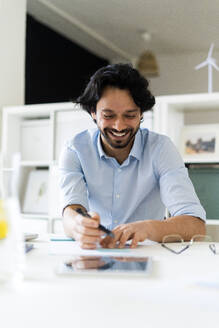 Lächelnder männlicher Unternehmer, der am Schreibtisch sitzt und arbeitet - GIOF12840