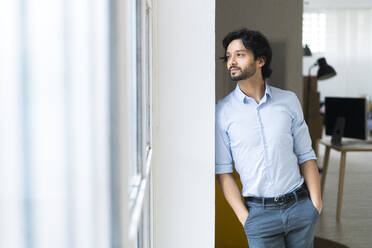 Thoughtful male entrepreneur with hands in pockets leaning on wall - GIOF12842