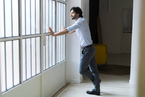Männlicher Unternehmer schaut weg, während er sich durch das Fenster lehnt - GIOF12843