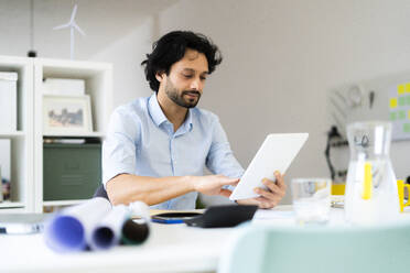 Junger männlicher Unternehmer, der ein digitales Tablet benutzt, während er im Büro sitzt - GIOF12852