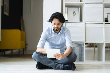 Männlicher Unternehmer, der ein digitales Tablet benutzt, während er im Büro auf dem Boden sitzt - GIOF12854