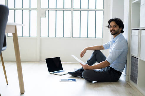 Männlicher Unternehmer mit digitalem Tablet und Laptop auf dem Boden sitzend im Büro - GIOF12856