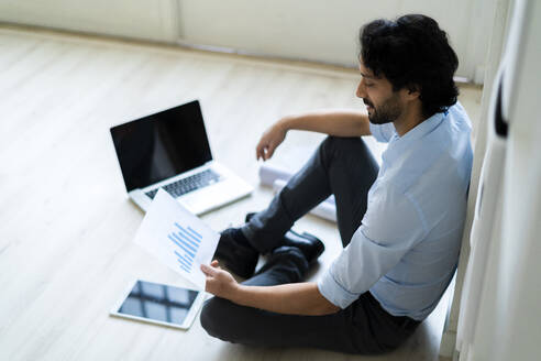 Geschäftsmann mit digitalem Tablet und Laptop, der ein grafisches Dokument im Büro analysiert - GIOF12857