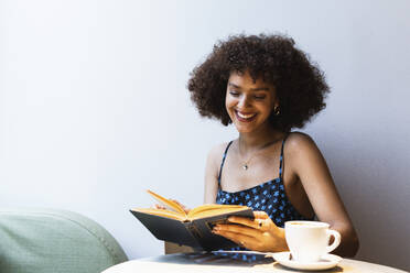 Lächelnder Universitätsstudent, der in einem Café ein Buch liest - PNAF01806