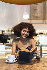 Lächelnde Frau, die in einem Café ein Buch liest - PNAF01809